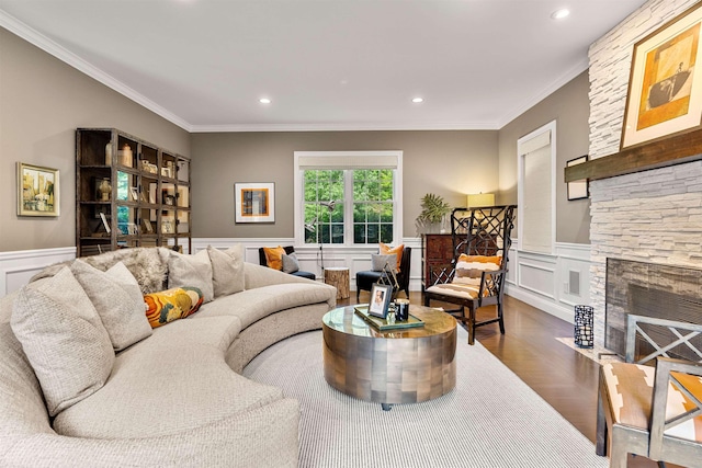 living room with wood finished floors, recessed lighting, a stone fireplace, wainscoting, and crown molding