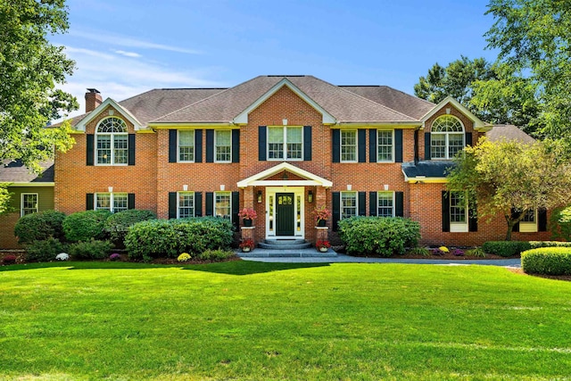 view of front facade with a front lawn, brick siding, and a chimney