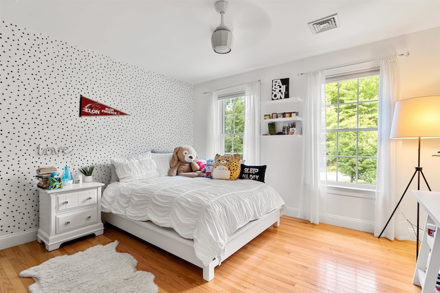 bedroom featuring wallpapered walls, baseboards, light wood finished floors, and an accent wall