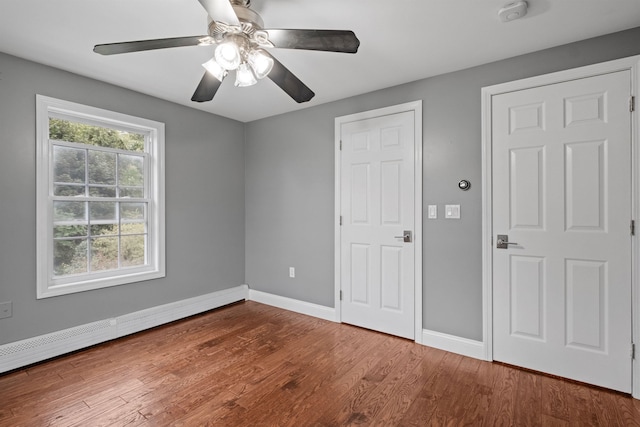 unfurnished bedroom with a baseboard heating unit, multiple windows, hardwood / wood-style floors, and ceiling fan