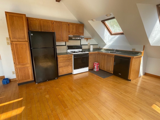 kitchen with light wood-type flooring, black appliances, vaulted ceiling with skylight, and sink