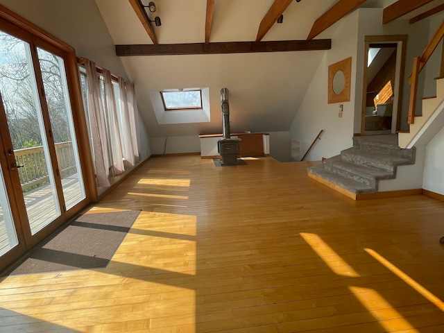 unfurnished living room featuring high vaulted ceiling, beam ceiling, a wood stove, and light hardwood / wood-style floors