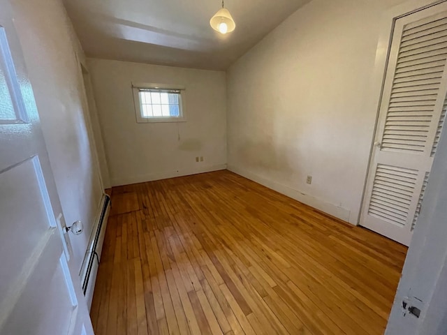 unfurnished bedroom featuring a baseboard heating unit, light wood-type flooring, a closet, and baseboards