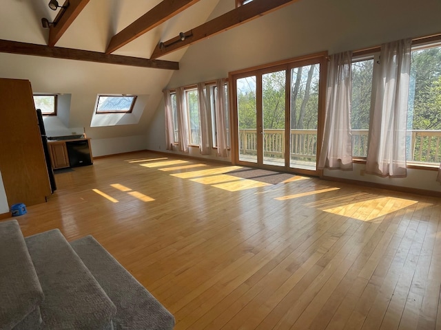 interior space with light wood-style floors, a wealth of natural light, beamed ceiling, and baseboards