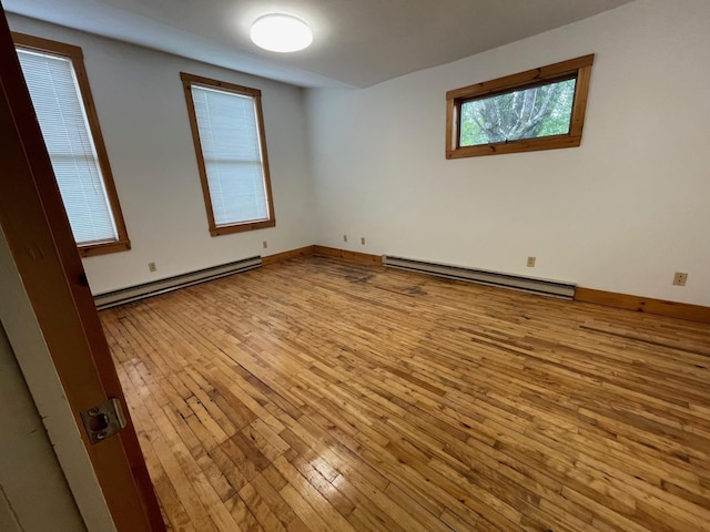 unfurnished room with wood-type flooring, a baseboard heating unit, and baseboards