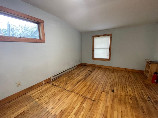 unfurnished room featuring a baseboard heating unit, light wood-style floors, and baseboards