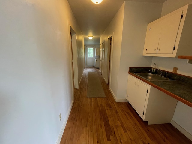 hallway with dark wood-style floors, a sink, and baseboards