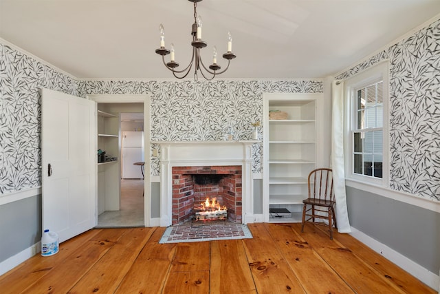 unfurnished living room featuring a fireplace, built in shelves, a chandelier, and wood-type flooring