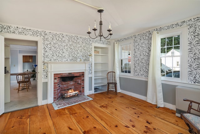 unfurnished living room with a fireplace, radiator heating unit, a notable chandelier, and light hardwood / wood-style floors