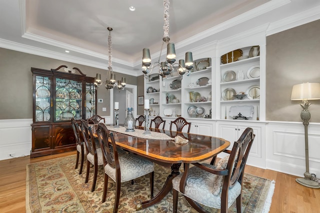 dining space featuring crown molding, light hardwood / wood-style flooring, a notable chandelier, and a tray ceiling