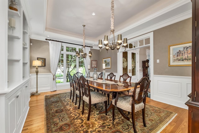 dining room featuring an inviting chandelier, a raised ceiling, crown molding, and light hardwood / wood-style flooring