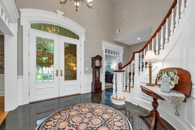 foyer entrance with an inviting chandelier, a towering ceiling, and french doors