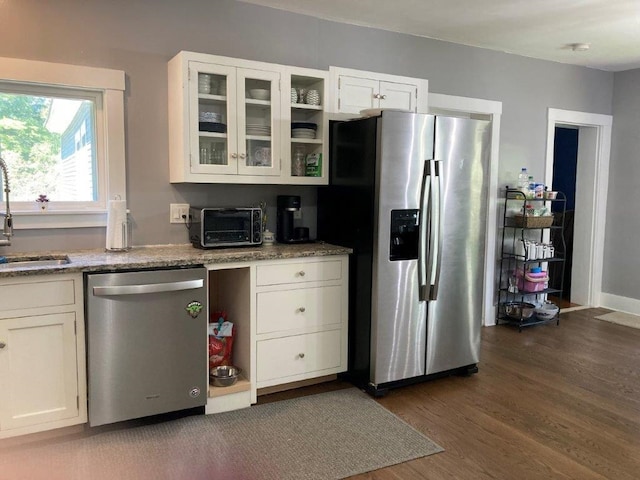 kitchen with light stone counters, sink, dark wood-type flooring, appliances with stainless steel finishes, and white cabinets