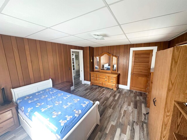 unfurnished bedroom with a closet, wood walls, a paneled ceiling, and dark hardwood / wood-style floors