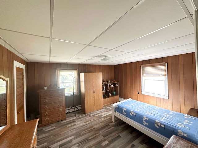 bedroom featuring a baseboard heating unit, dark hardwood / wood-style flooring, and wooden walls