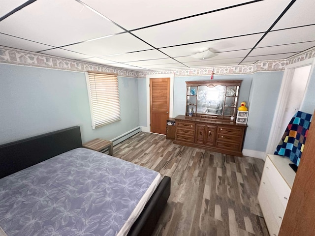 bedroom featuring a baseboard radiator, multiple windows, hardwood / wood-style flooring, and a drop ceiling