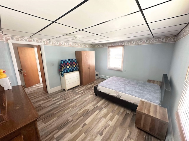 bedroom featuring a baseboard heating unit, hardwood / wood-style floors, and a drop ceiling