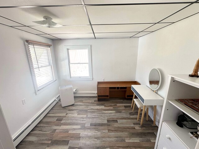 unfurnished office featuring dark wood-type flooring, a baseboard heating unit, and a drop ceiling