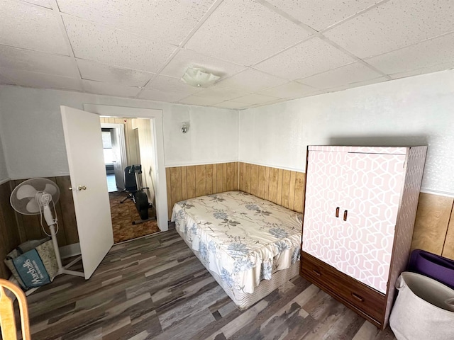 bedroom featuring wood walls, dark hardwood / wood-style flooring, and a drop ceiling