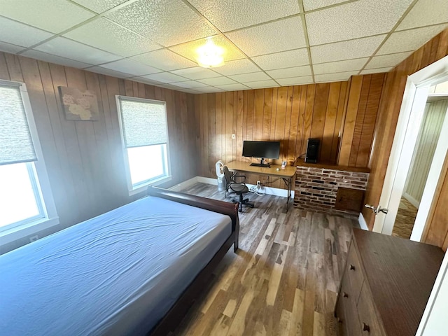 bedroom featuring wood walls, hardwood / wood-style flooring, and a drop ceiling