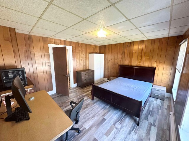 bedroom with a paneled ceiling, hardwood / wood-style floors, and wood walls