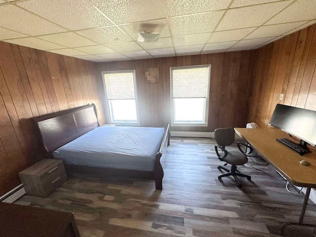 bedroom with wood walls, baseboard heating, a paneled ceiling, and dark hardwood / wood-style floors