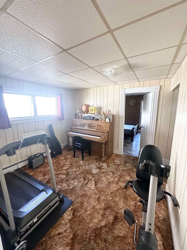 workout room with a paneled ceiling, carpet flooring, wooden walls, and a baseboard heating unit