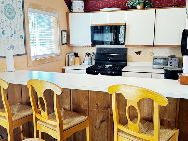 kitchen featuring white cabinets, a kitchen bar, and black appliances