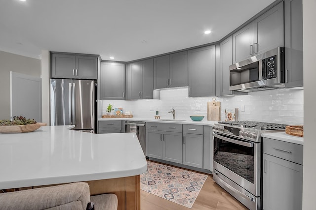 kitchen with sink, backsplash, gray cabinets, appliances with stainless steel finishes, and light wood-type flooring