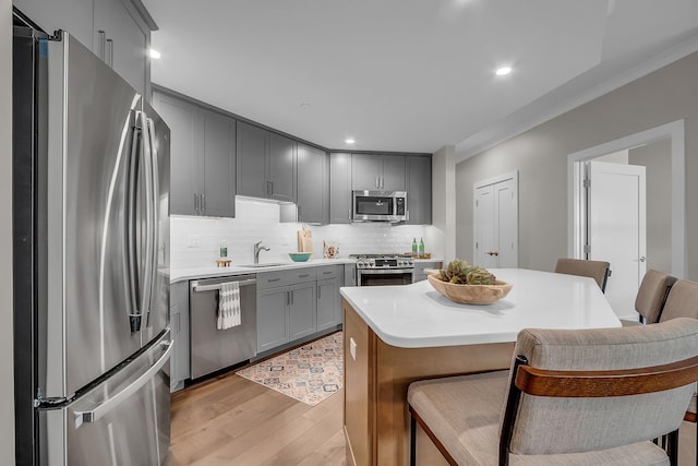 kitchen featuring sink, backsplash, stainless steel appliances, a breakfast bar area, and light hardwood / wood-style floors