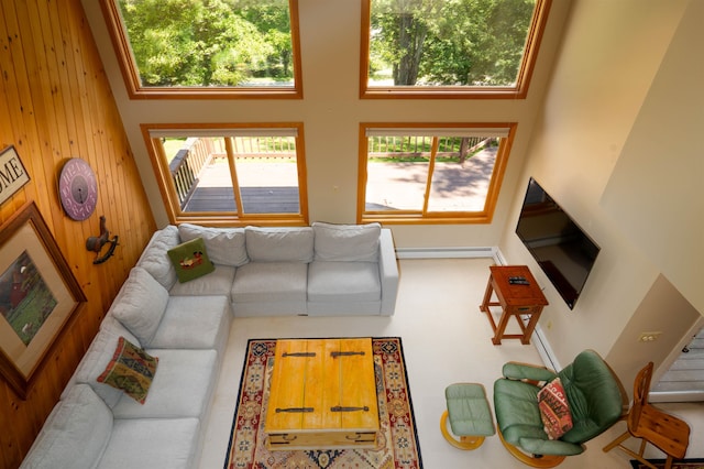 living room featuring a towering ceiling, baseboard heating, and wooden walls