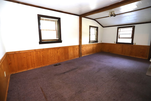 carpeted spare room featuring a wealth of natural light, wood walls, and beam ceiling