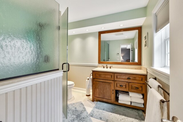 bathroom featuring toilet, a stall shower, recessed lighting, wainscoting, and vanity