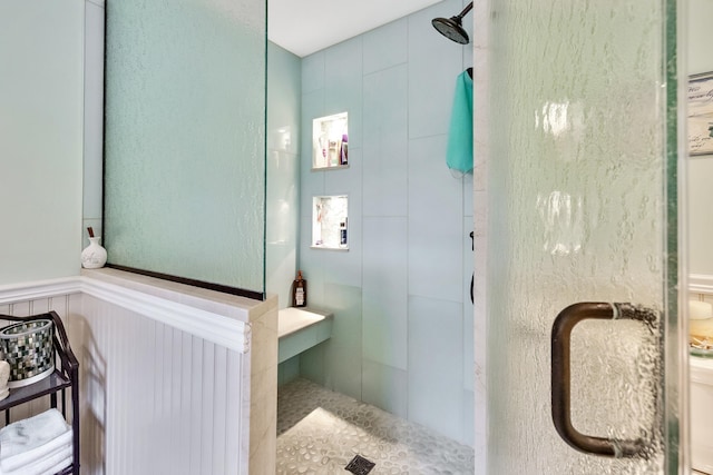 bathroom with a wainscoted wall and a shower stall