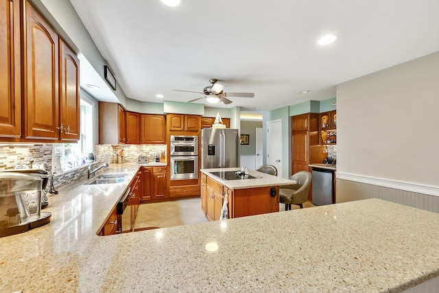 kitchen with backsplash, light stone countertops, a wainscoted wall, stainless steel appliances, and a sink