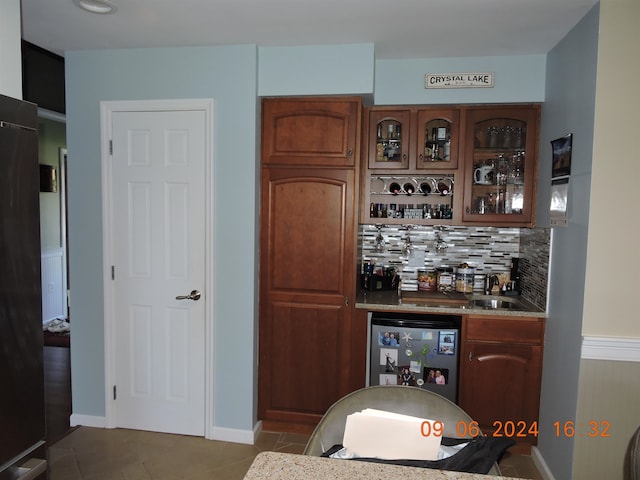 bar featuring stainless steel fridge, decorative backsplash, light tile patterned flooring, and sink