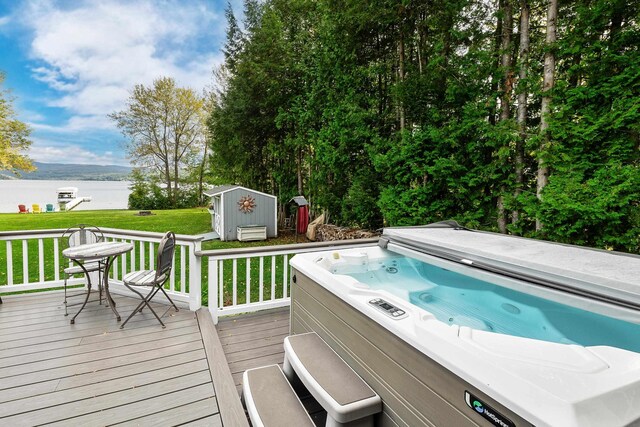 deck featuring a water view, a lawn, a storage shed, and a hot tub