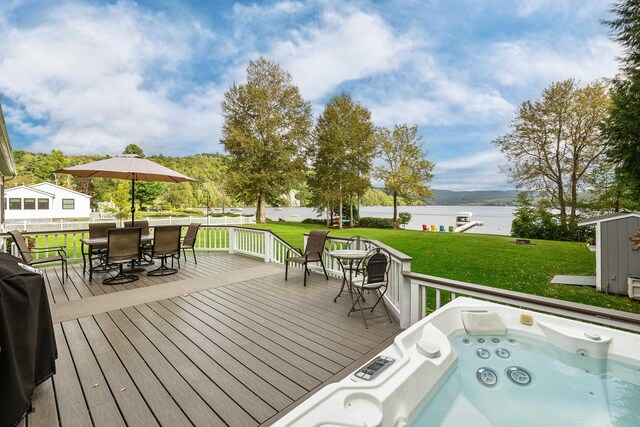 wooden terrace featuring a yard, a water view, a shed, and an outdoor hot tub