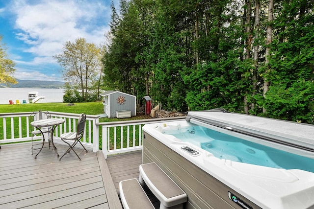 wooden deck featuring a hot tub, a water view, a lawn, a storage shed, and an outdoor structure