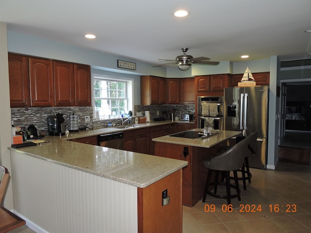 kitchen featuring appliances with stainless steel finishes, a center island, a breakfast bar, sink, and ceiling fan