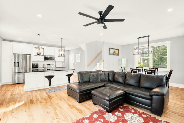 living room with ceiling fan with notable chandelier and light hardwood / wood-style floors