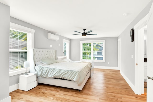 bedroom featuring a wall mounted AC, multiple windows, ceiling fan, and light hardwood / wood-style floors