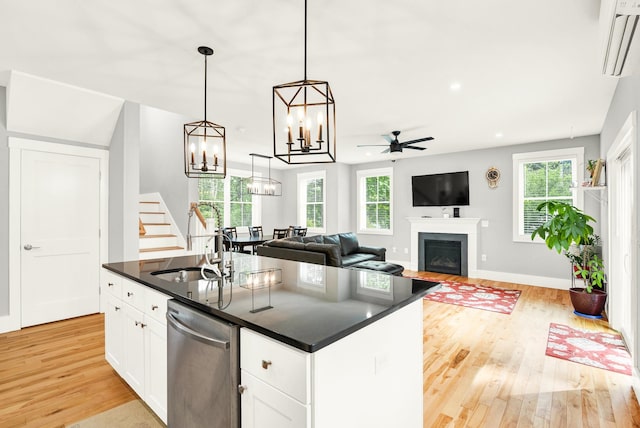 kitchen with a healthy amount of sunlight, ceiling fan with notable chandelier, white cabinetry, dishwasher, and a center island with sink