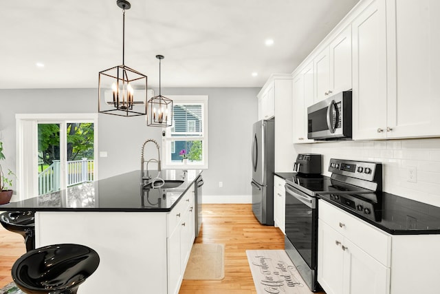 kitchen with white cabinets, appliances with stainless steel finishes, light hardwood / wood-style floors, sink, and a kitchen island with sink