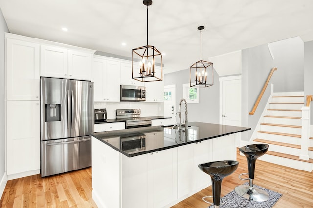 kitchen with pendant lighting, stainless steel appliances, a center island with sink, and light hardwood / wood-style flooring