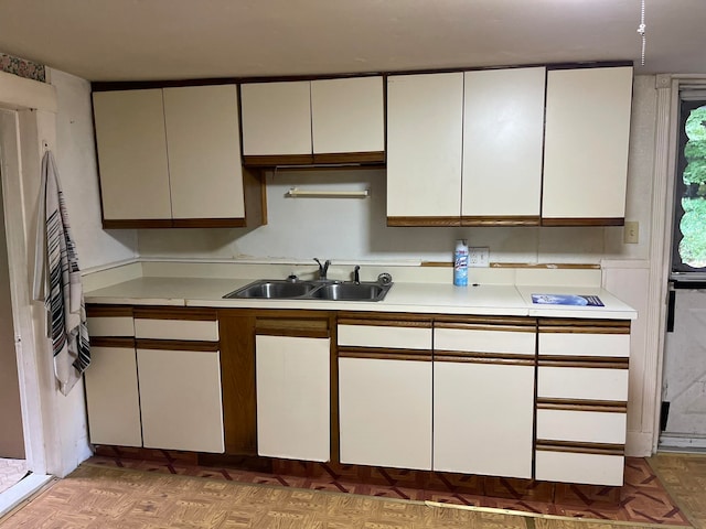 kitchen with parquet flooring, white cabinetry, and sink