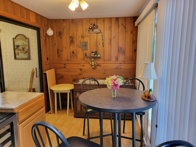 dining room with beverage cooler, wooden walls, and light hardwood / wood-style flooring