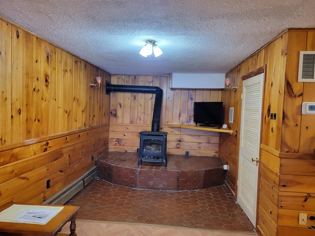 living room with a wood stove, wood walls, a baseboard heating unit, and a textured ceiling