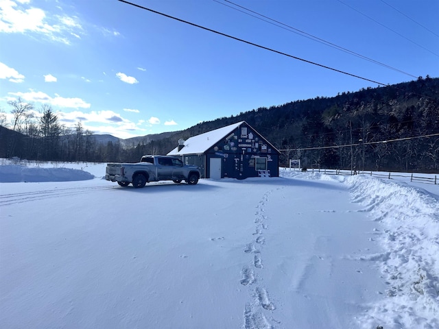 snowy yard featuring a mountain view, a view of trees, and an outbuilding