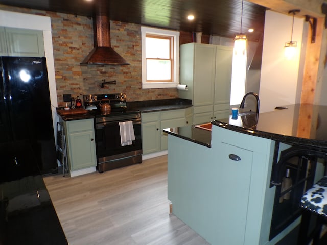 kitchen featuring stainless steel range with electric stovetop, black fridge, decorative light fixtures, wall chimney exhaust hood, and light hardwood / wood-style floors